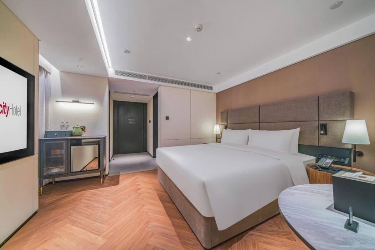 Ein Hotelzimmer mit Bett, Nachttisch, Lampe und Schreibtisch mit Stuhl.