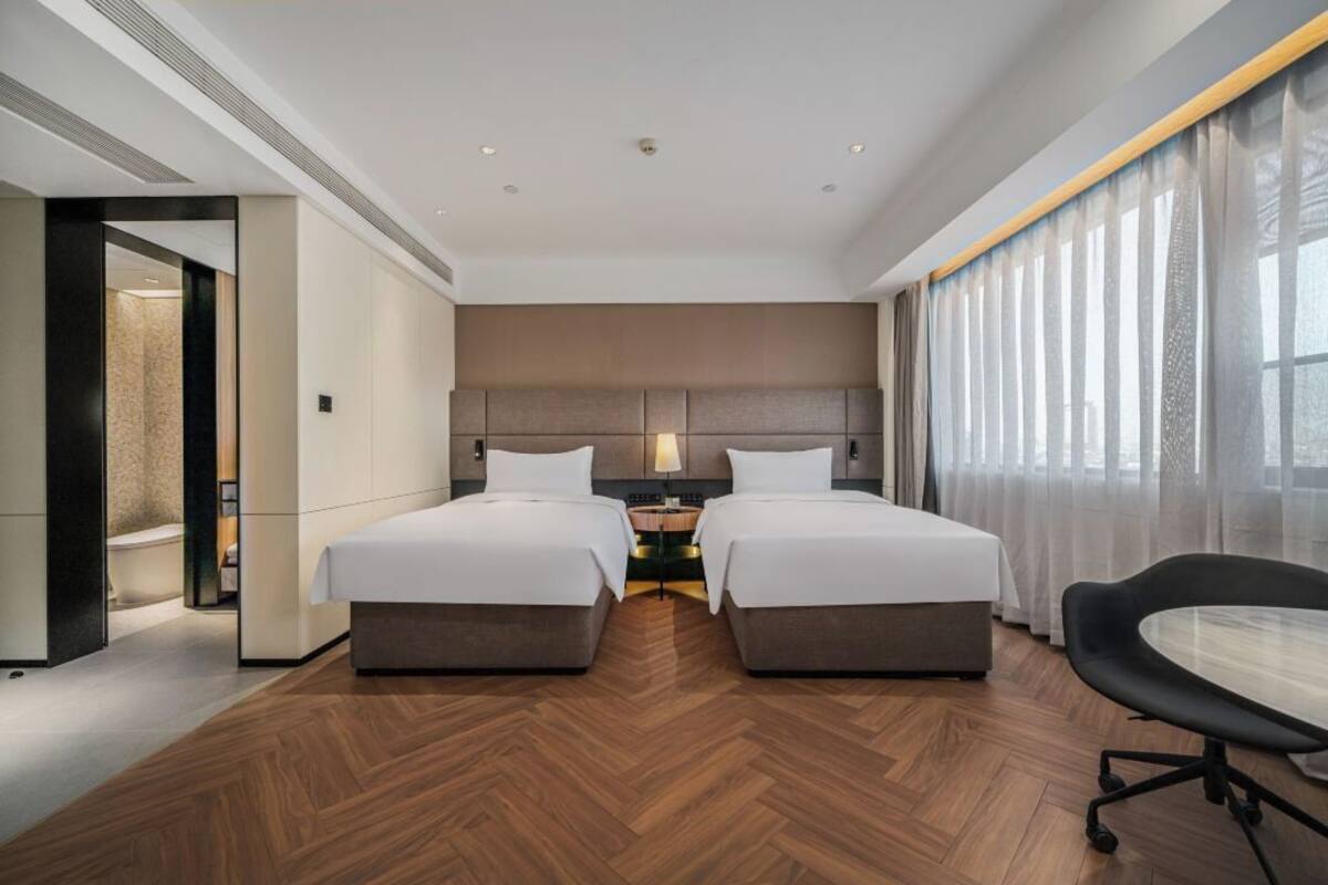 Ein modernes Hotelzimmer mit zwei Betten, einem Schreibtisch und einem Stuhl.