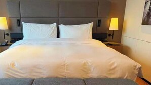 Una habitación de hotel con una cama grande, dos lámparas de noche, una mesita de noche y un cabecero.