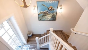 A staircase with white railings, a painting of sea turtles, and a chandelier.
