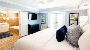 A bedroom with a bed, a ceiling fan, a TV, a door, and a window.
