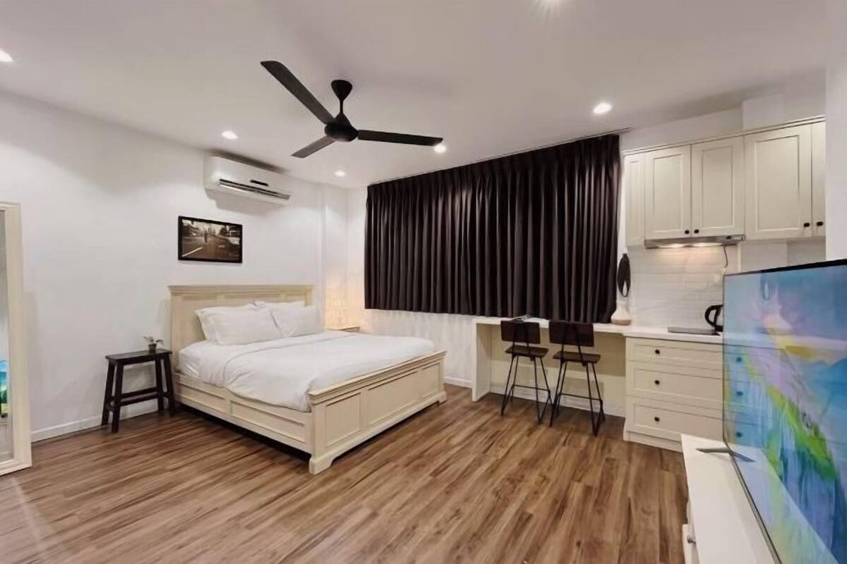 A bedroom with a bed, a desk, a chair, a ceiling fan, and a painting.