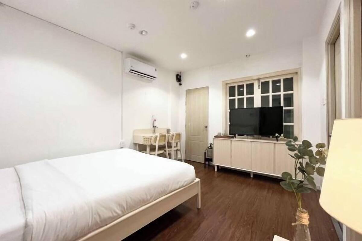 A bedroom with a bed, a desk, a chair, a TV, and a window.