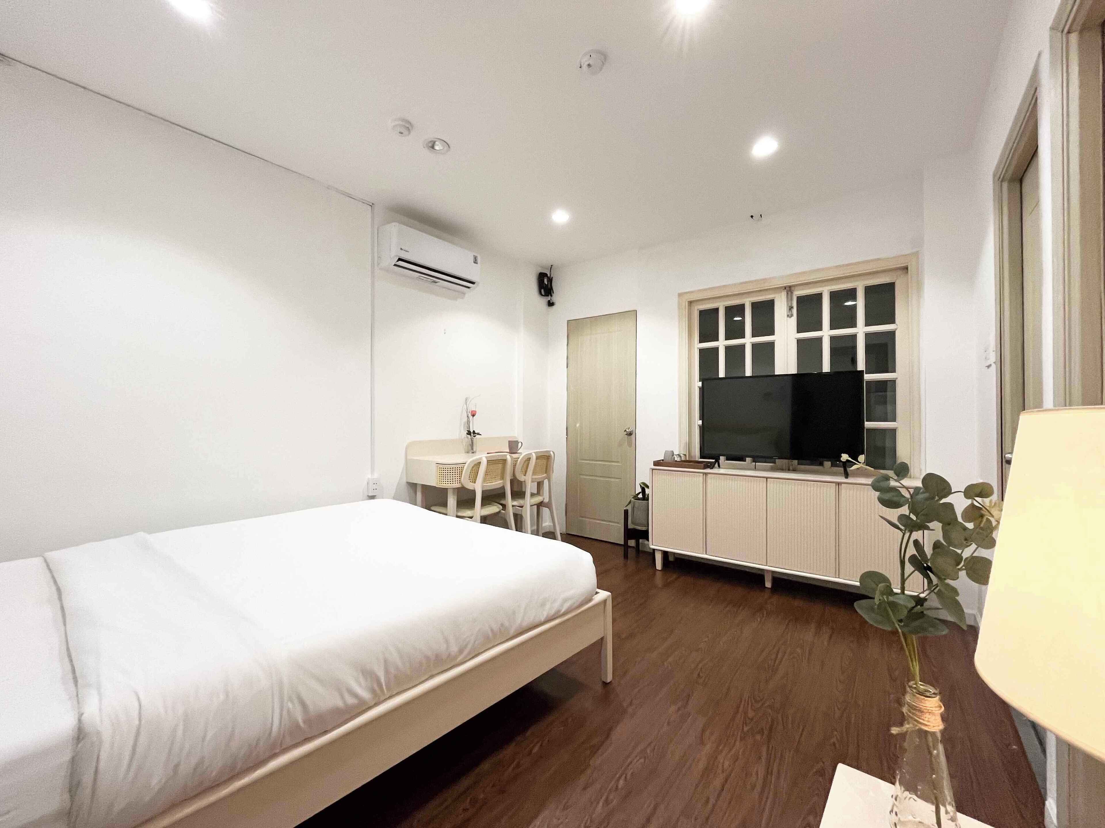 A modern hotel room with a single bed, a small dining table, a TV on a cabinet, and a potted plant.