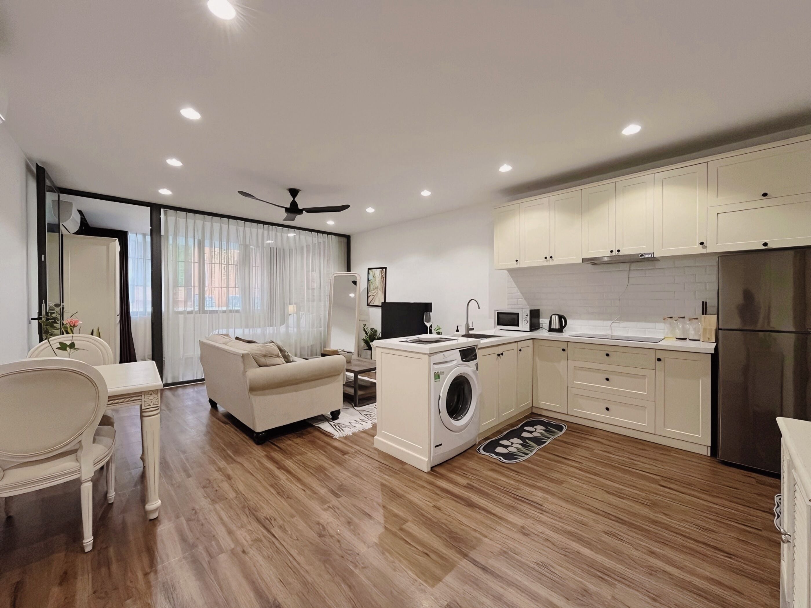 A modern kitchen with a built-in washer, a dining area with a white table and chairs, and a living room with a sofa and a TV.