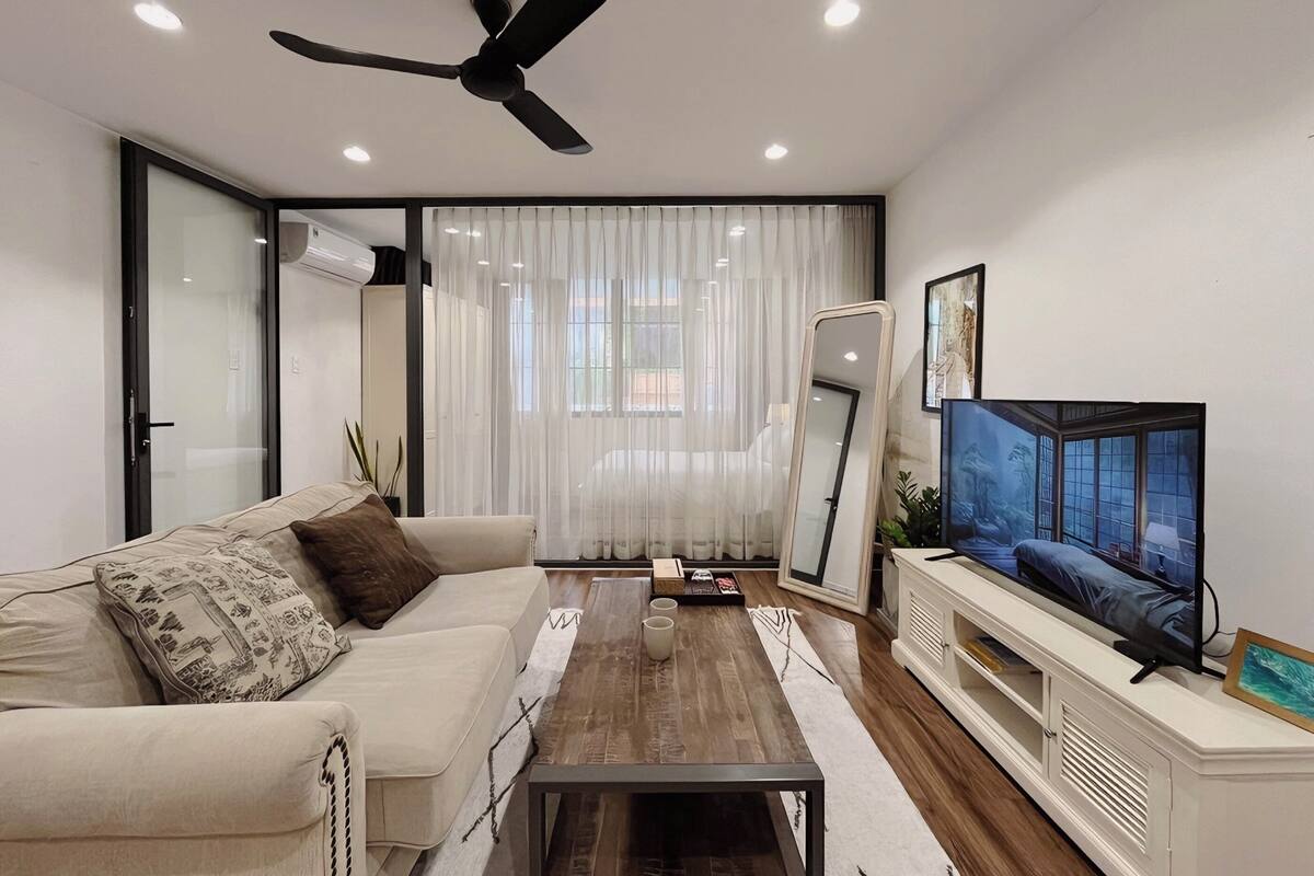 A modern living room with a sofa, coffee table, TV, and ceiling fan.