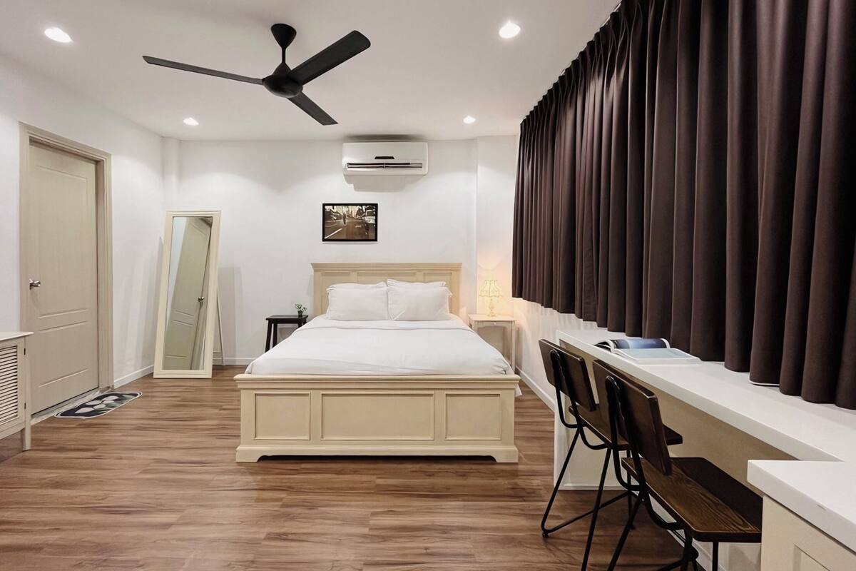 A hotel room with a bed, a desk, a chair, a ceiling fan, and a window with curtains.