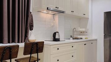 A modern kitchen with white cabinets, a stainless steel range hood, a kettle, and a refrigerator.