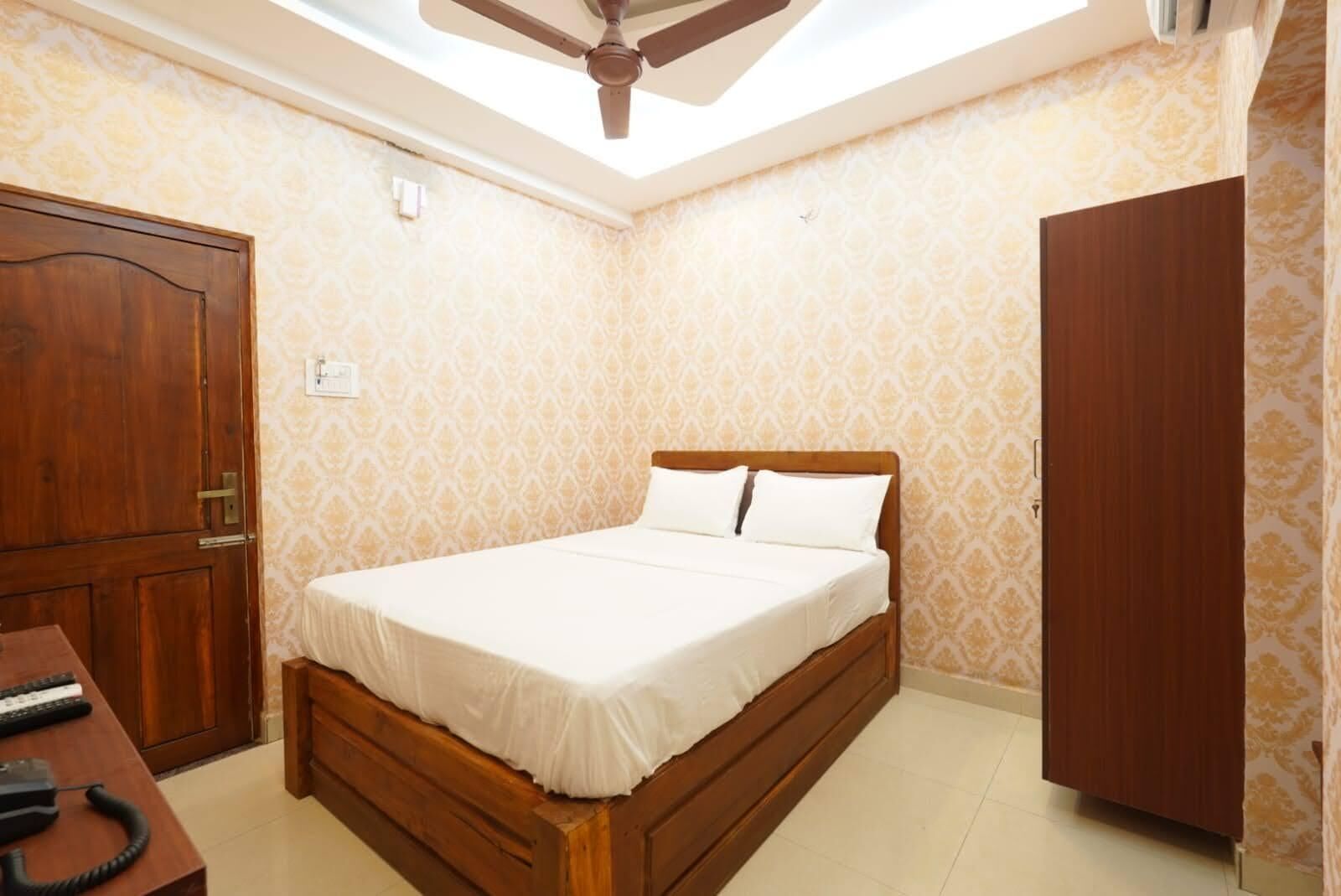 A bedroom with a wooden bed, a desk with a telephone, and a wardrobe.