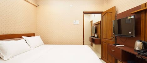 A hotel room with a bed, a television, a desk with a kettle, and a mirror.