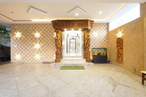 Un vestíbulo con pared de diseño a cuadros, suelo de mármol y una escalera central que conduce a un nivel superior.