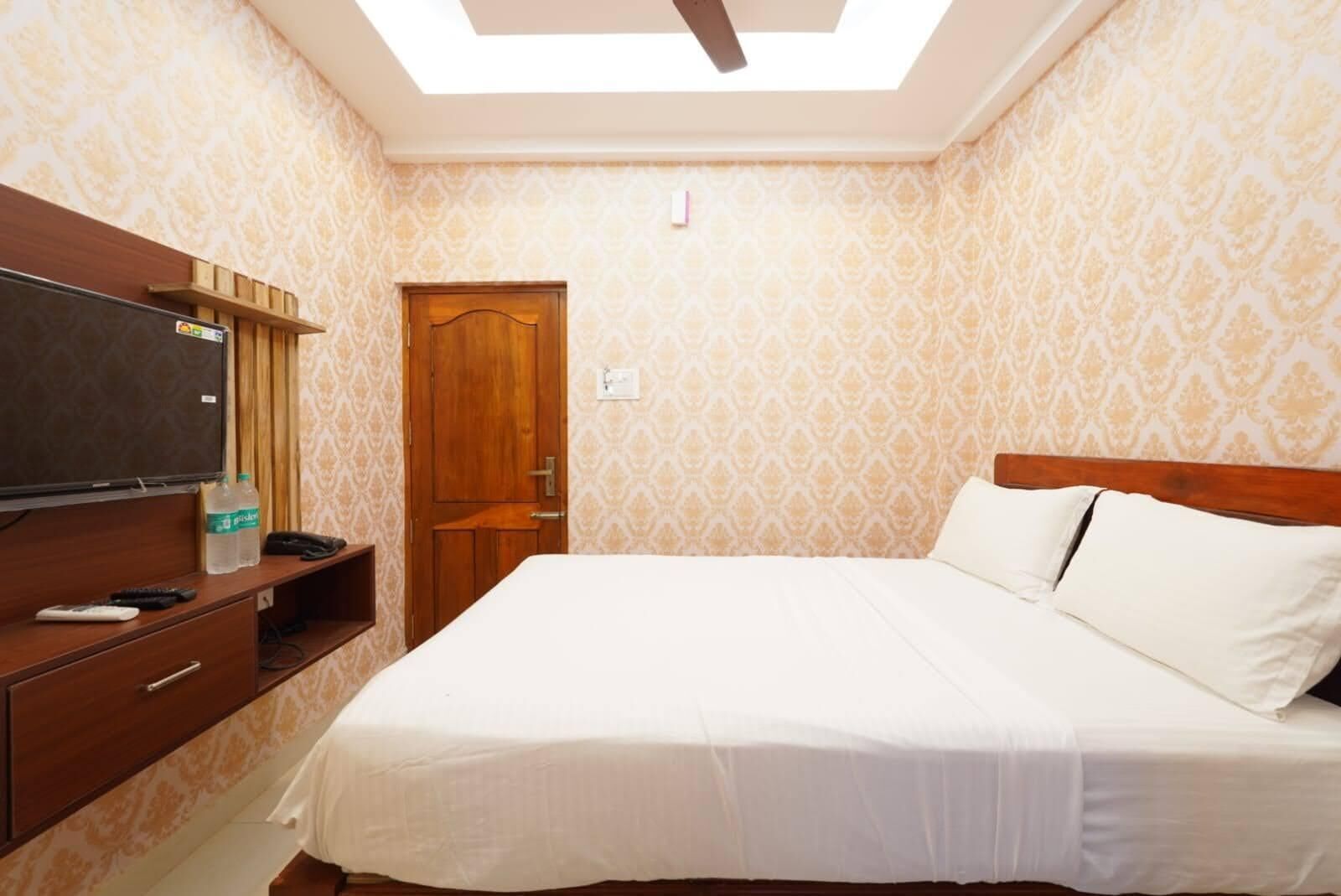 A hotel room with a bed, a TV, a wooden wardrobe, and a door.