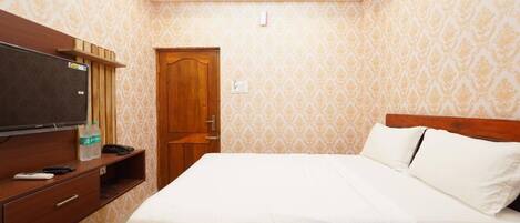 A hotel room with a bed, a TV, a wooden wardrobe, and a door.