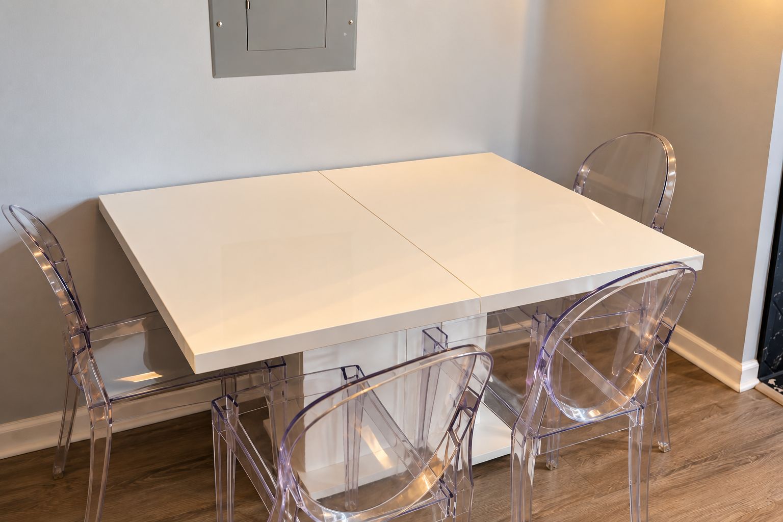 Une table de salle à manger blanche, accompagnée de quatre chaises transparentes.