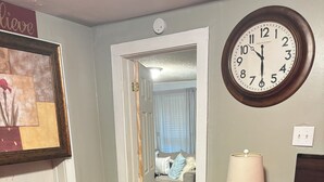 A bedroom with a bed, a nightstand, a lamp, a clock, a stool, and a door leading to another room. - Comfortable 2BR Retreat in Ruston Perfect for Game Days” (Ruston)