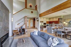 A spacious living area with a fireplace, a staircase, a dining area, and a kitchen. - NEW 5 Mins to Gondola Golf Course, Private Hot Tub (Whistler)
