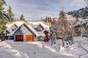A house with a sloped roof, wooden garage doors, and snow-covered surroundings. - NEW 5 Mins to Gondola Golf Course, Private Hot Tub (Whistler)