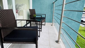 A balcony with wicker furniture, a small table, and a potted plant. - Vive Luxe Condo , Pool & 24/7 Security near Airport (D'Abadie)