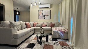 A living room with a beige sectional sofa, a glass coffee table, and a patterned rug. - Vive Luxe Condo , Pool & 24/7 Security near Airport (D'Abadie)