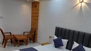 A modern bedroom with a bed, wooden chairs, a small table, and a ceiling fan. - Hotel The Grand Jashi Residency (Patan)
