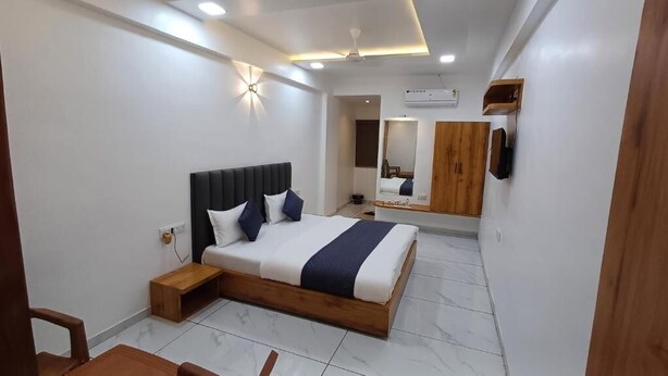 A modern bedroom with a large bed, bedside tables, a mirror, and a ceiling fan. - Hotel The Grand Jashi Residency (Patan)