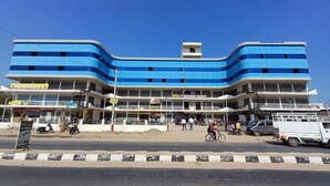 A multi-story hotel with a blue facade, a visible entrance, and a Renault dealership across the street. - Hotel The Grand Jashi Residency (Patan)