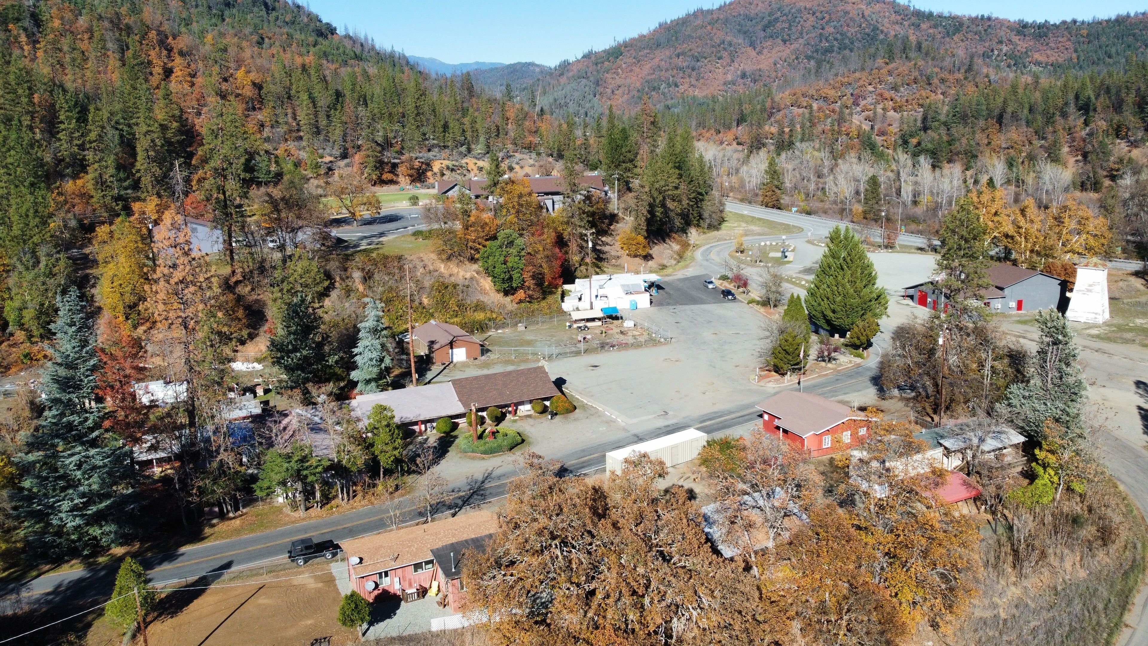 An aerial view of a small town with a mix of residential and commercial buildings, surrounded by forested hills.