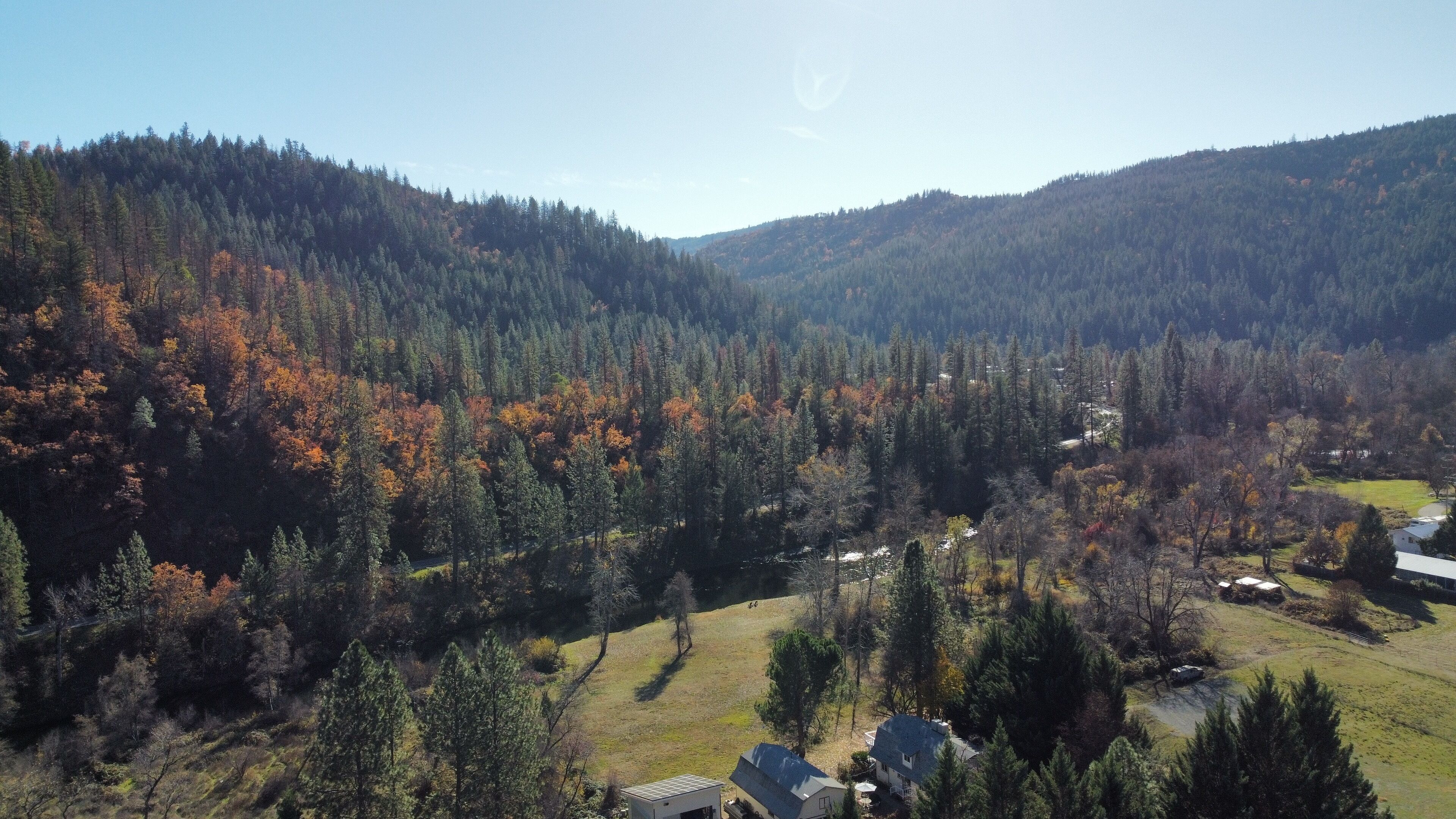 A rural landscape with a house surrounded by dense forest and hills.
