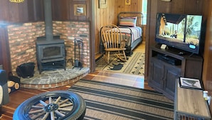A rustic room with a brick fireplace, a television, a rocking chair, and a bed with striped bedding.