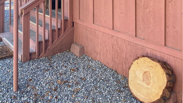 A wooden cabin with a porch, a staircase, and a large saw blade sign on the wall.