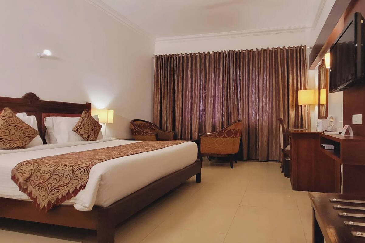 A hotel room with a large bed, a desk with a lamp, a chair, and a television on the wall.