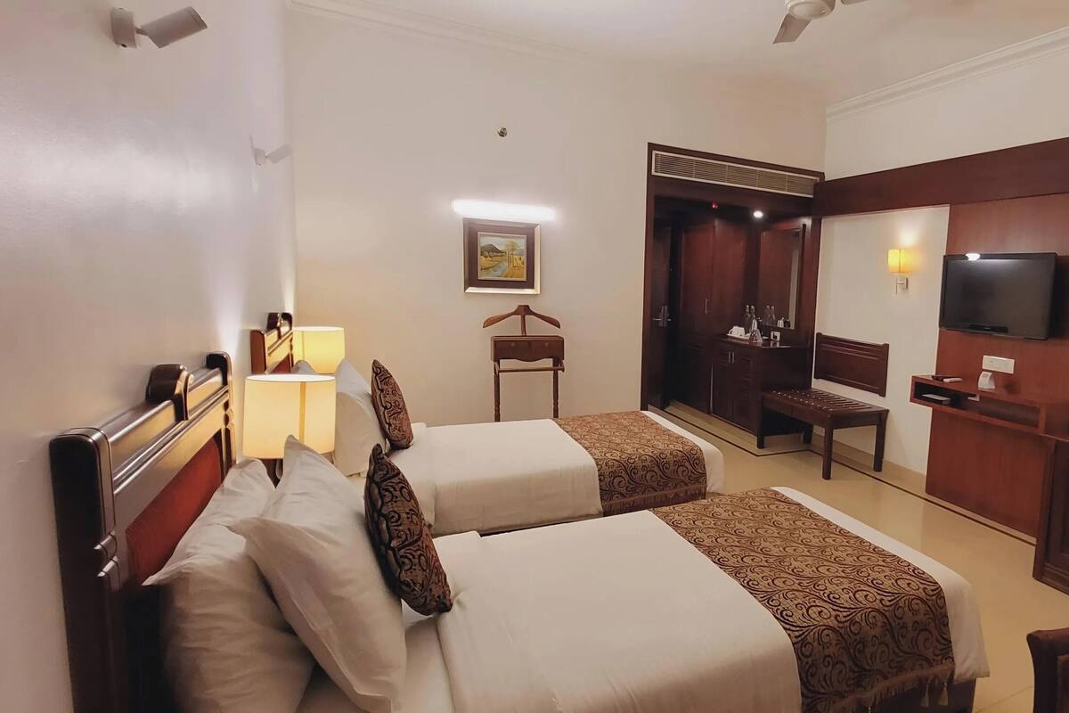 A hotel room with two beds, a desk, a chair, a TV, and a mirror.
