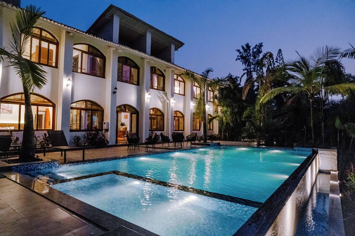 A large outdoor swimming pool surrounded by palm trees and a multi-story building with balconies.
