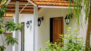 A white building with a tiled roof, a wooden door, and a white railing. - Aeraki palms (Dahanu)