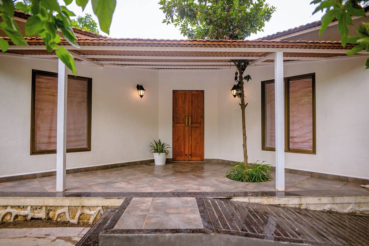 A covered outdoor area with a tiled floor, a wooden door, and two wall-mounted lights.