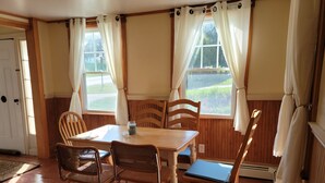 Un comedor con una mesa de madera y cuatro sillas, una ventana con cortinas y una puerta.