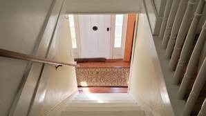 Una escalera conduce a una habitación con una alfombra estampada y una puerta blanca.