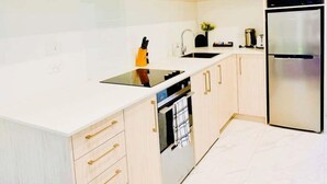 Een moderne keuken met lichte houten kastjes, een wit aanrecht, een ingebouwde oven en een roestvrijstalen koelkast.