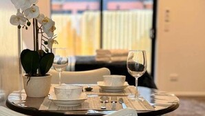 Een eettafel gedekt met witte borden, kommen en een wijnglas, met een potorkidee erbij.