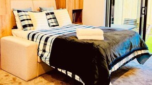 Een moderne slaapkamer met een houten hoofdbord, een bed met gestreept beddengoed en uitzicht op een gebouw door een glazen deur.