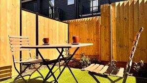 Een terras met een houten tafel en stoelen, omgeven door een houten hek en een gebouw met ramen.