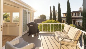 An open patio with a white sofa, a grill, and a baby stroller. - Springcombe Sunset - St Heliers Beach House (Auckland)