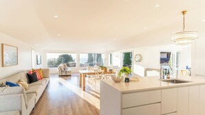 A spacious living area with a dining table, sofa, and kitchen island. - Springcombe Sunset - St Heliers Beach House (Auckland)