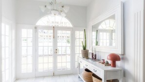 A bright room with white walls, a white console table, a mirror, and a door leading outside. - Springcombe Sunset - St Heliers Beach House (Auckland)