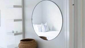 A room with a large oval mirror on the wall, a bed with white bedding, and a small shelf with decorative items. - Springcombe Sunset - St Heliers Beach House (Auckland)