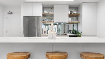 A modern kitchen with white cabinetry, a stainless steel refrigerator, and wooden stools.