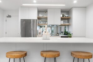 A modern kitchen with white cabinetry, a stainless steel refrigerator, and wooden stools. - City Escape - Newcastle CBD - Location Location (Newcastle)