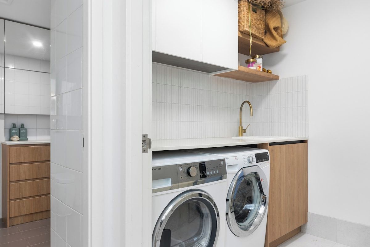 Un área de lavandería moderna con lavadora, pileta y muebles de madera.