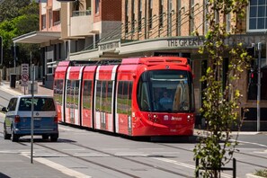 Un tramway rouge circule dans une rue de la ville, et on aperçoit en arrière-plan un bâtiment portant l’inscription « The Great Southern House ».