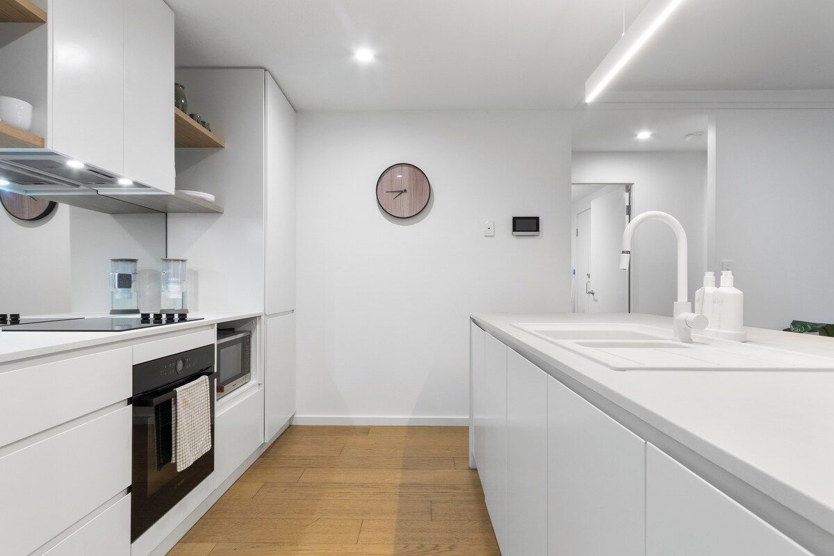A modern kitchen with white cabinetry, a built-in oven, a microwave, and a stainless steel range hood.
